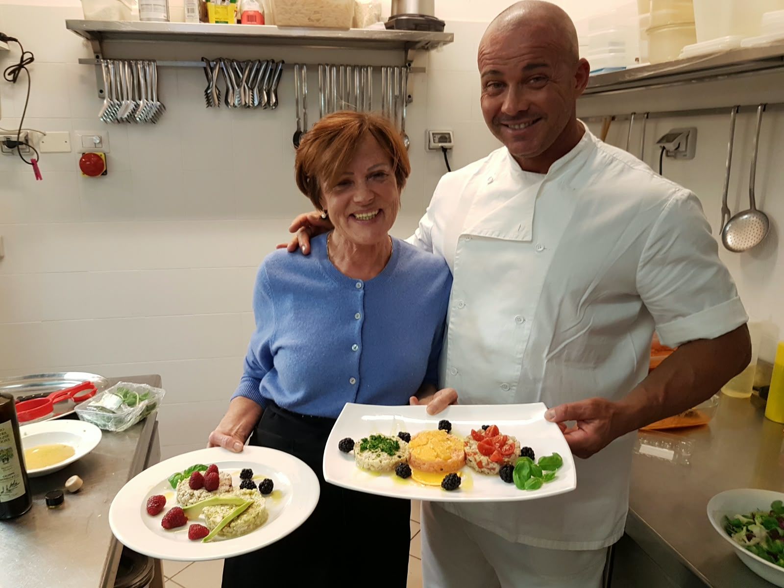 A woman and the cook in the kitchen, each holding a dish they have just plated.