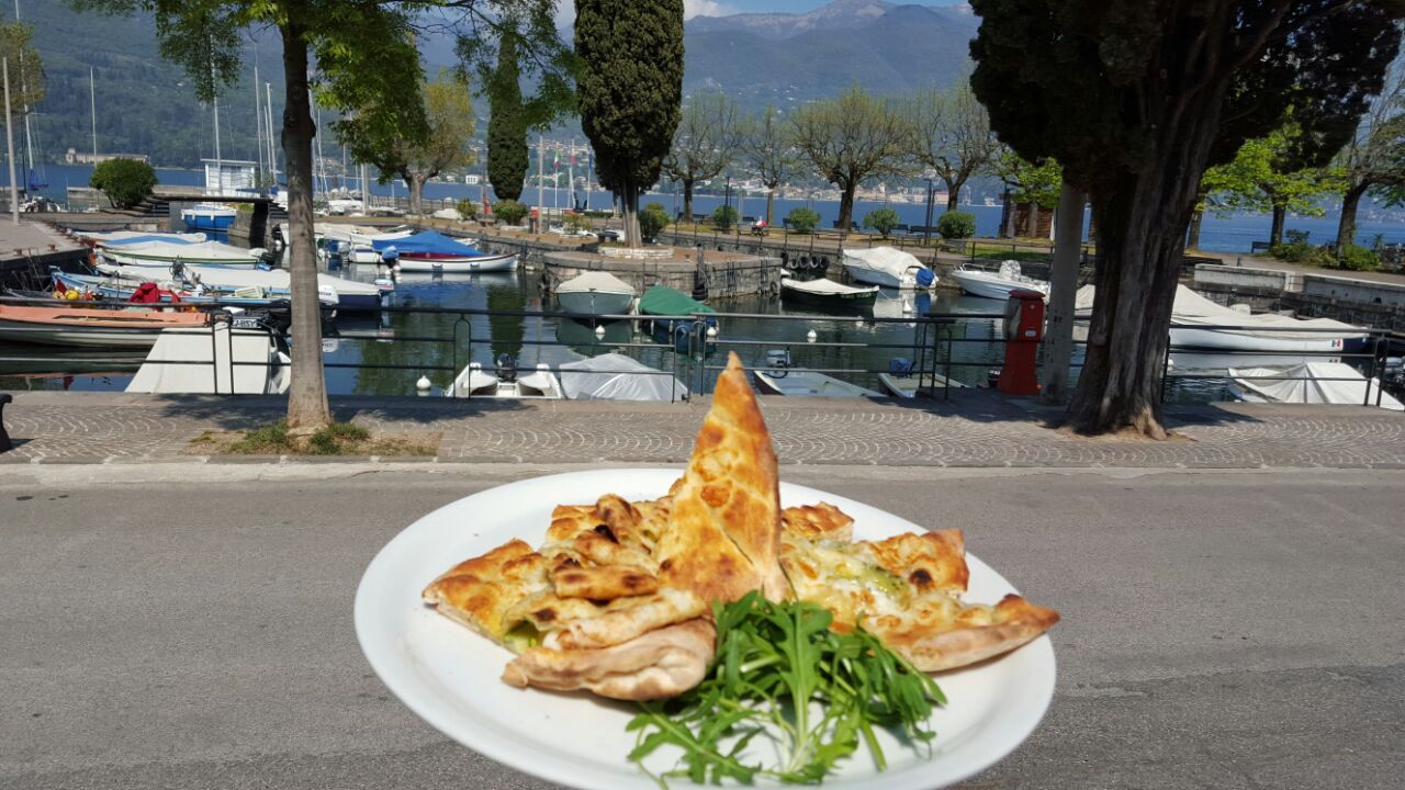 Ein am Tisch serviertes Gericht, dahinter der Hafen und die Boote.