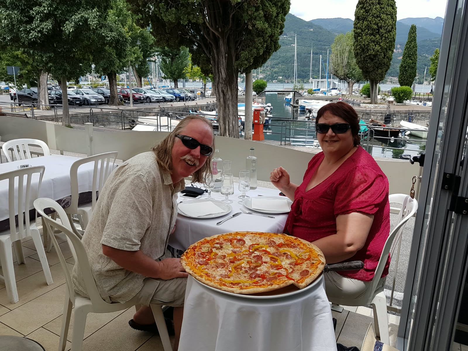 Zwei Gäste an einem Terrassentisch mit einer Pizza, mit Blick auf den Hafen.