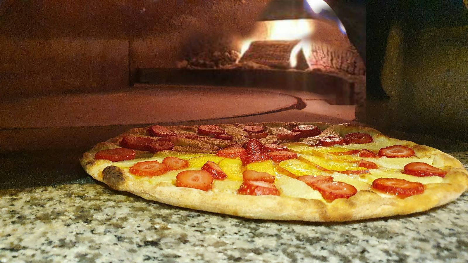 Eine Pizza im Holzofen, dahinter die Glut.