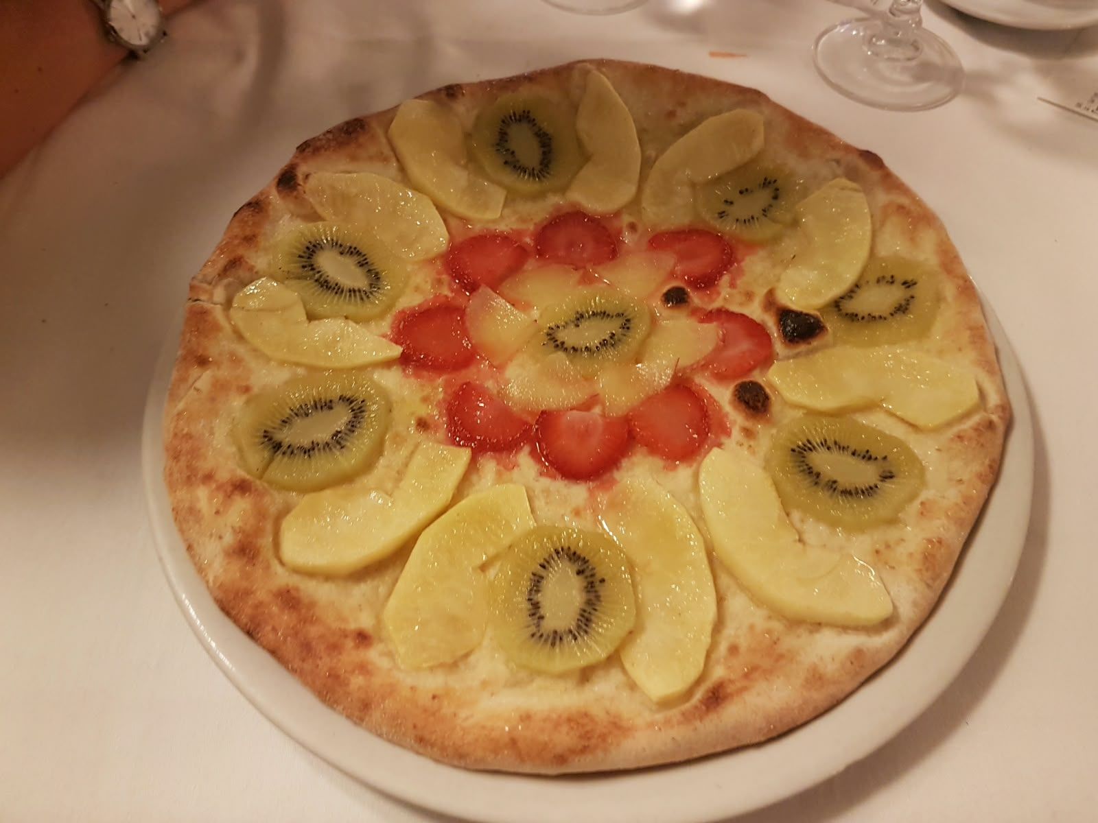 Süße Obstpizza mit Pfirsichen, Kiwi und Erdbeeren, kreisförmig angeordnet.