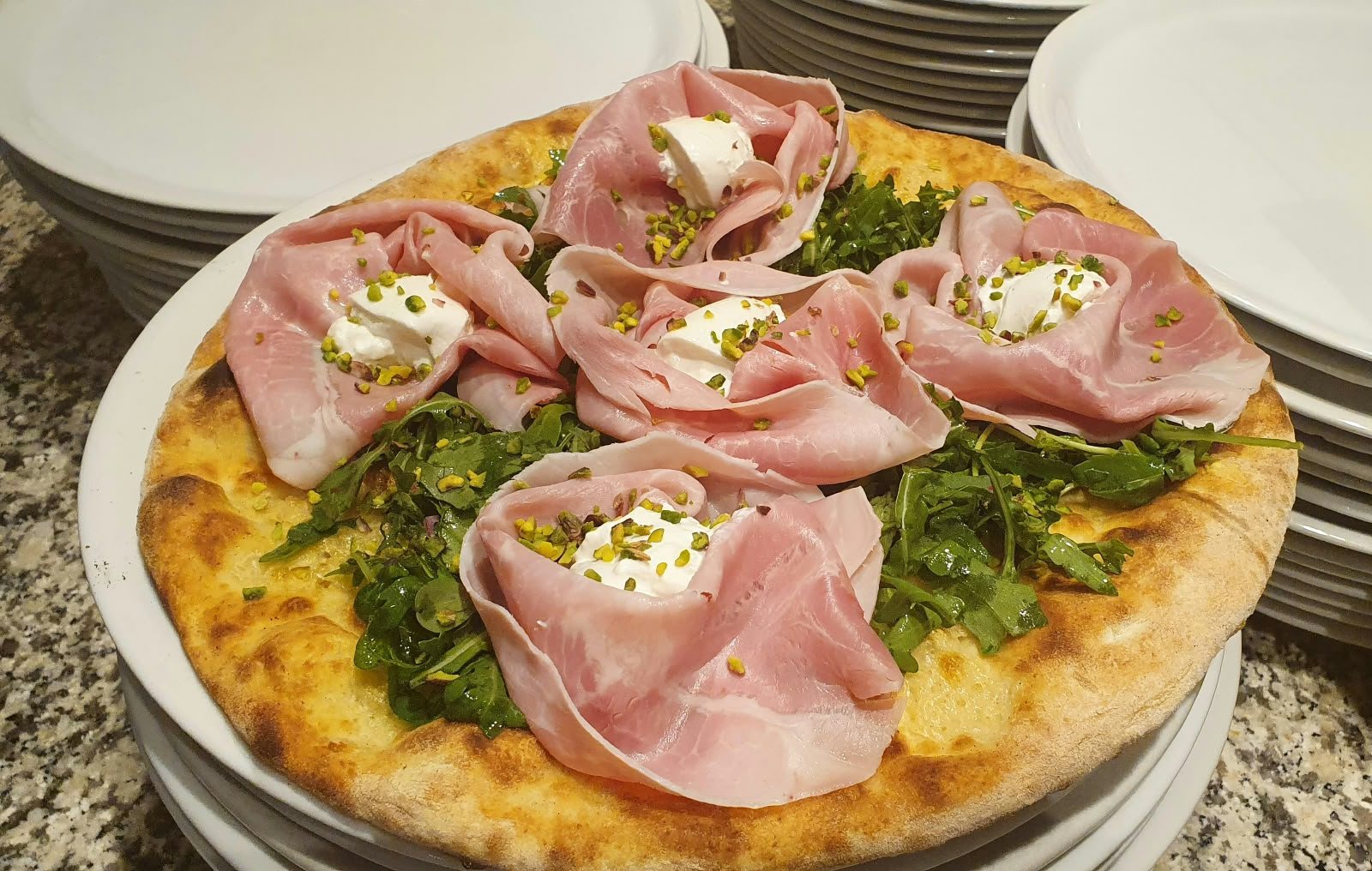 Eine Pizza mit Aufschnitt-Rosetten, Burrata und Pesto.