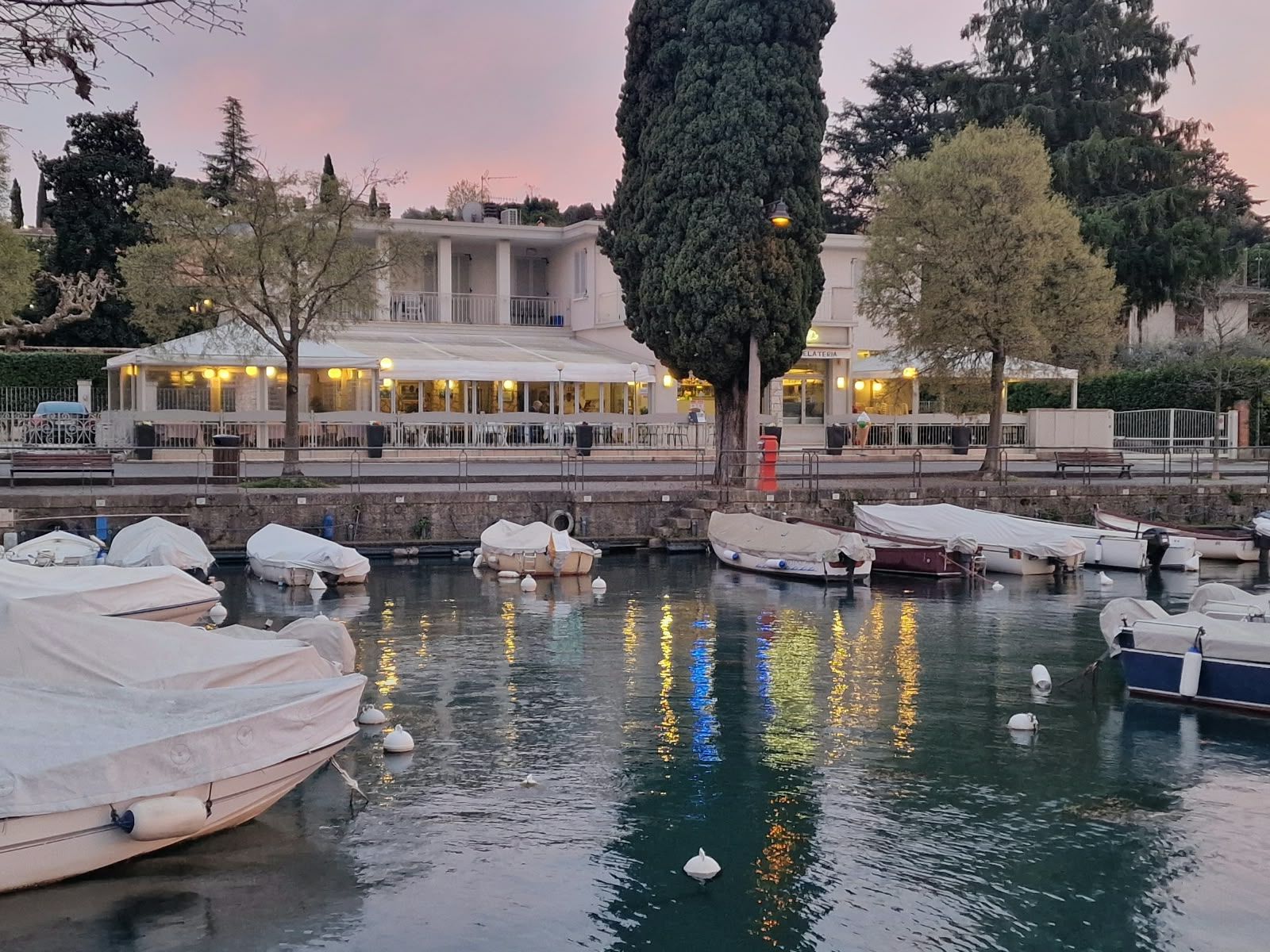 Gran Fausto seen from the harbour at Portese at dusk, its windows lit and the boats moored.