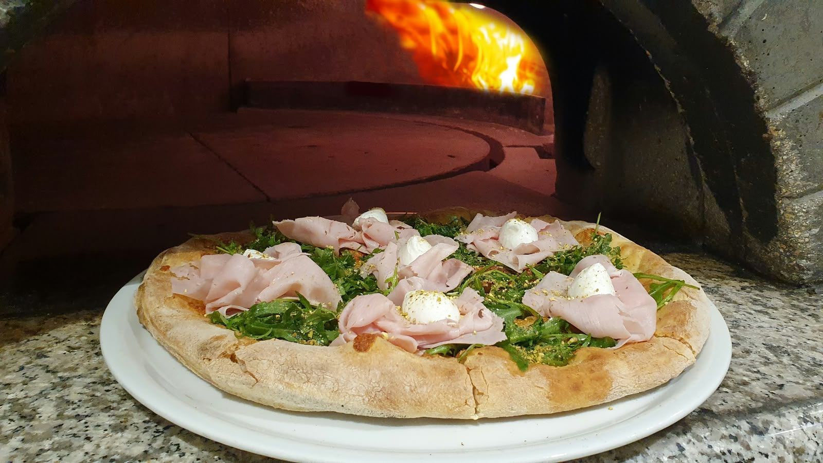 Eine frisch gebackene Pizza vor der Öffnung des brennenden Holzofens.