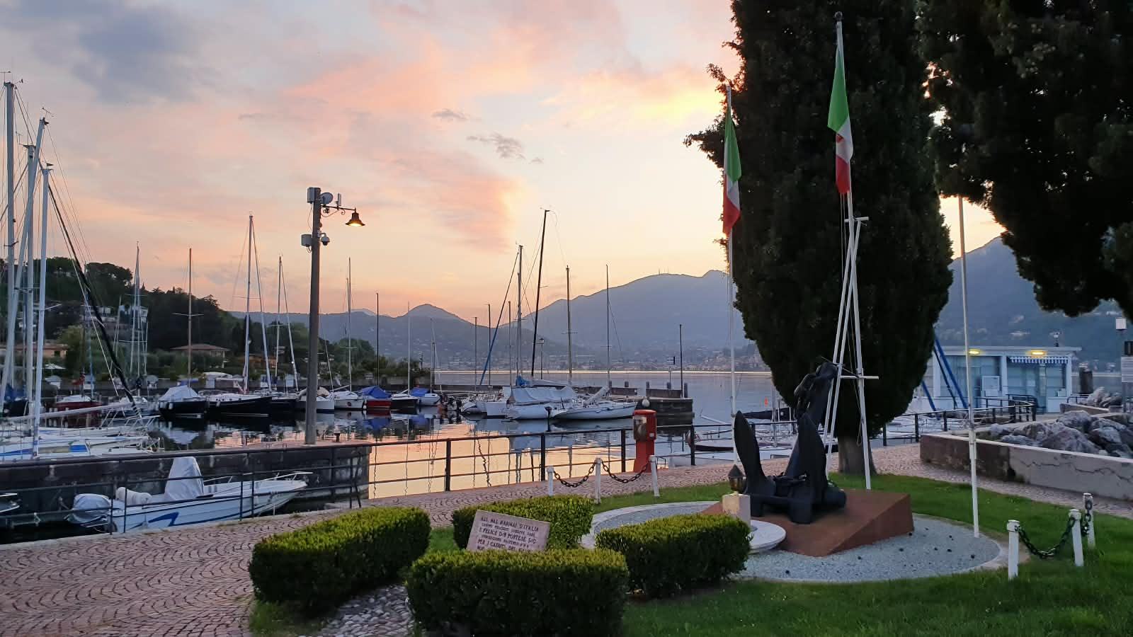The harbour at sunset: an anchor on a stone plinth, the flags and the moored boats.